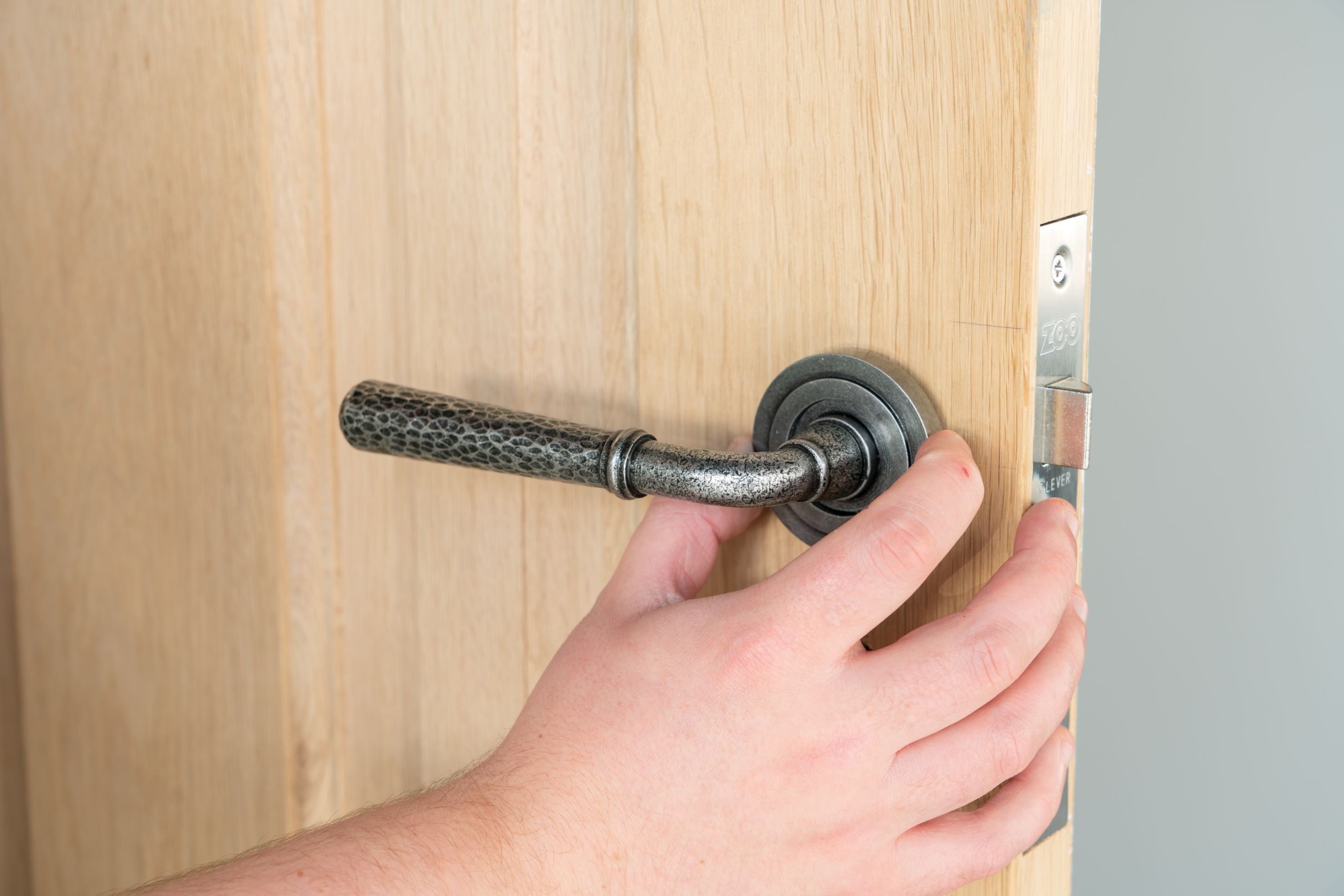 Person fitting a round escutcheon cover to a pewter lever on rose door handle on a wooden door.
