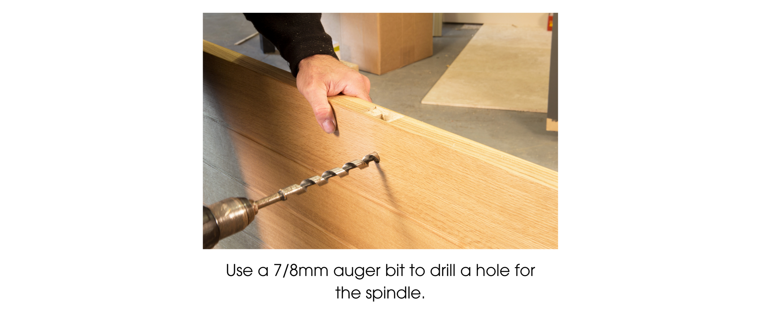 Person using an auger drill bit to drill a hole through a wooden door for a spindle to pass.