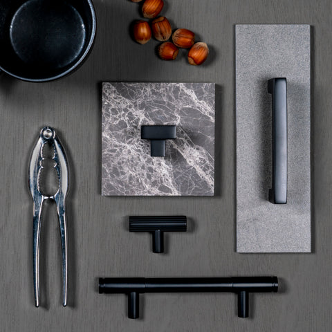 Grey moodboard with From The Anvil's Matt Black T Bar pull handles, cabinet handles, and cabinet pull handles with grey marble, a silver nutcracker, nuts, and a small black bowl.
