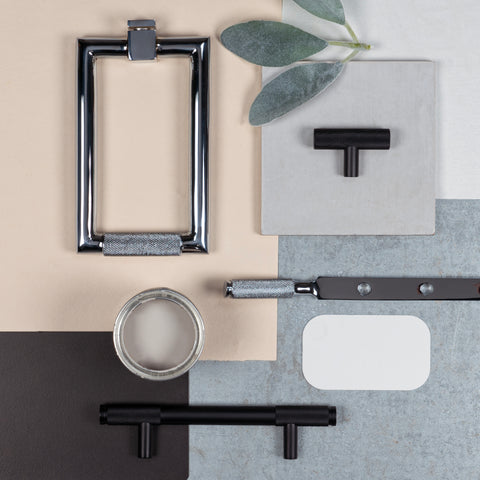 A moodboard of From The Anvil's Polished Chrome and Matt Black knurled Brompton hardware including a pull handle, window stay, t-bar cabinet pull handle, and a knurled door knocker, on beige, grey and black backgrounds, with a eucalyptus leaf and open pot of pink paint.