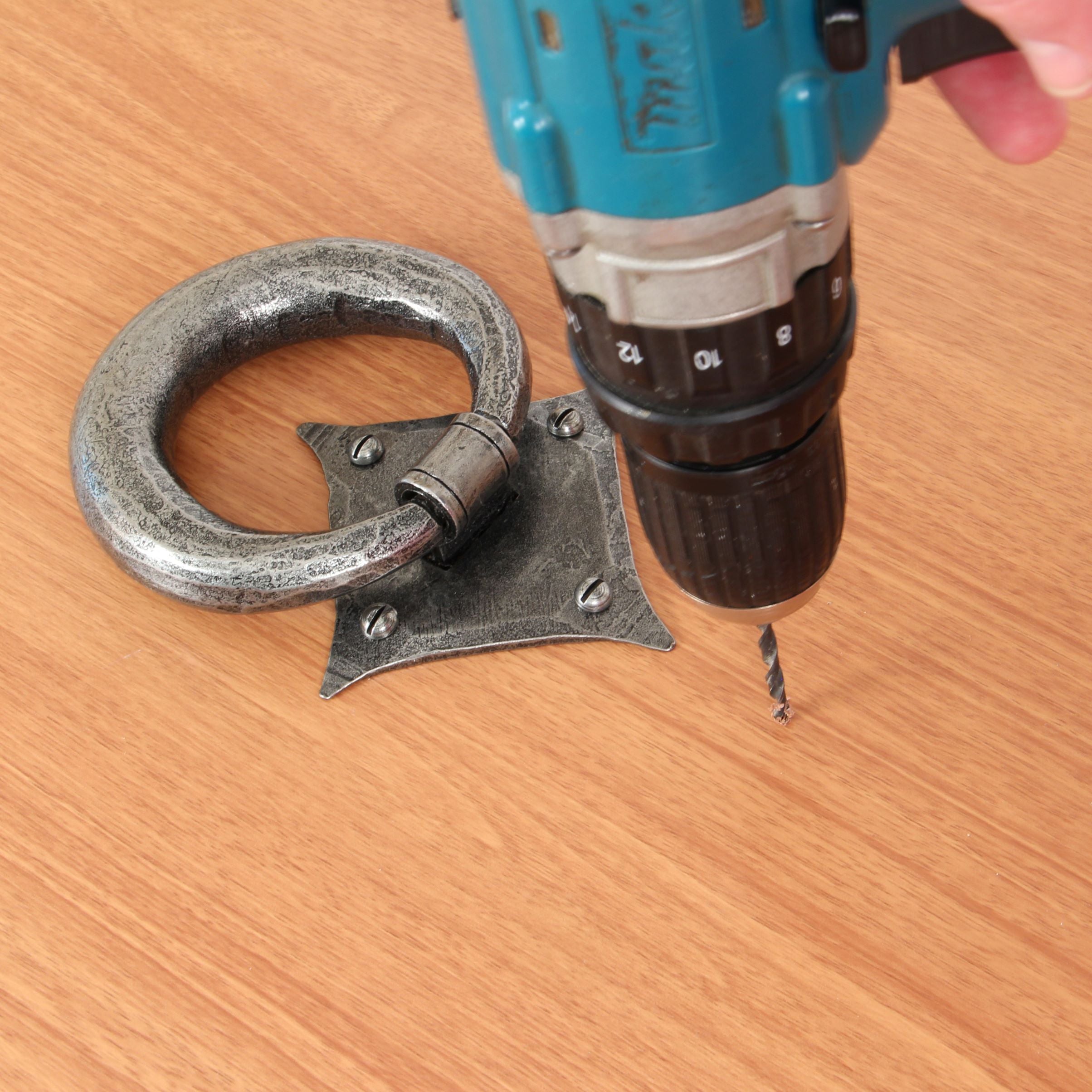 Person using an electric drill to drill a pilot hole in a wooden door for a strike plate.