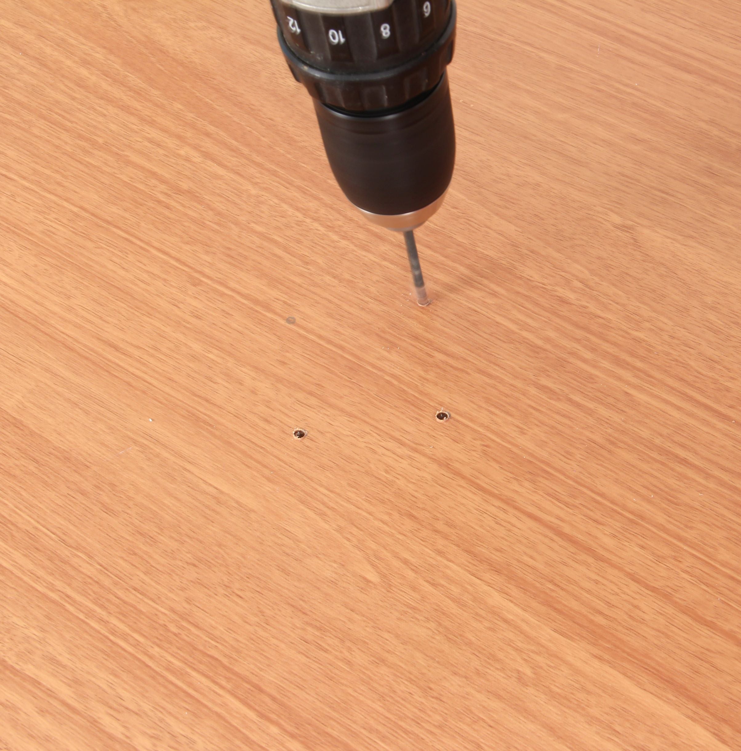 Person using an electric drill to screw four screw holes into a wooden door to fit a door knocker,