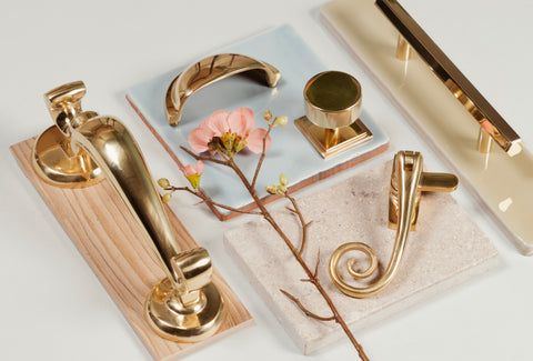 Moodboard of From The Anvil's Polished Brass hardware including door knocker, drawer pull, cabinet pull, window hardware, and pastel coloured tiles and a pink flower.