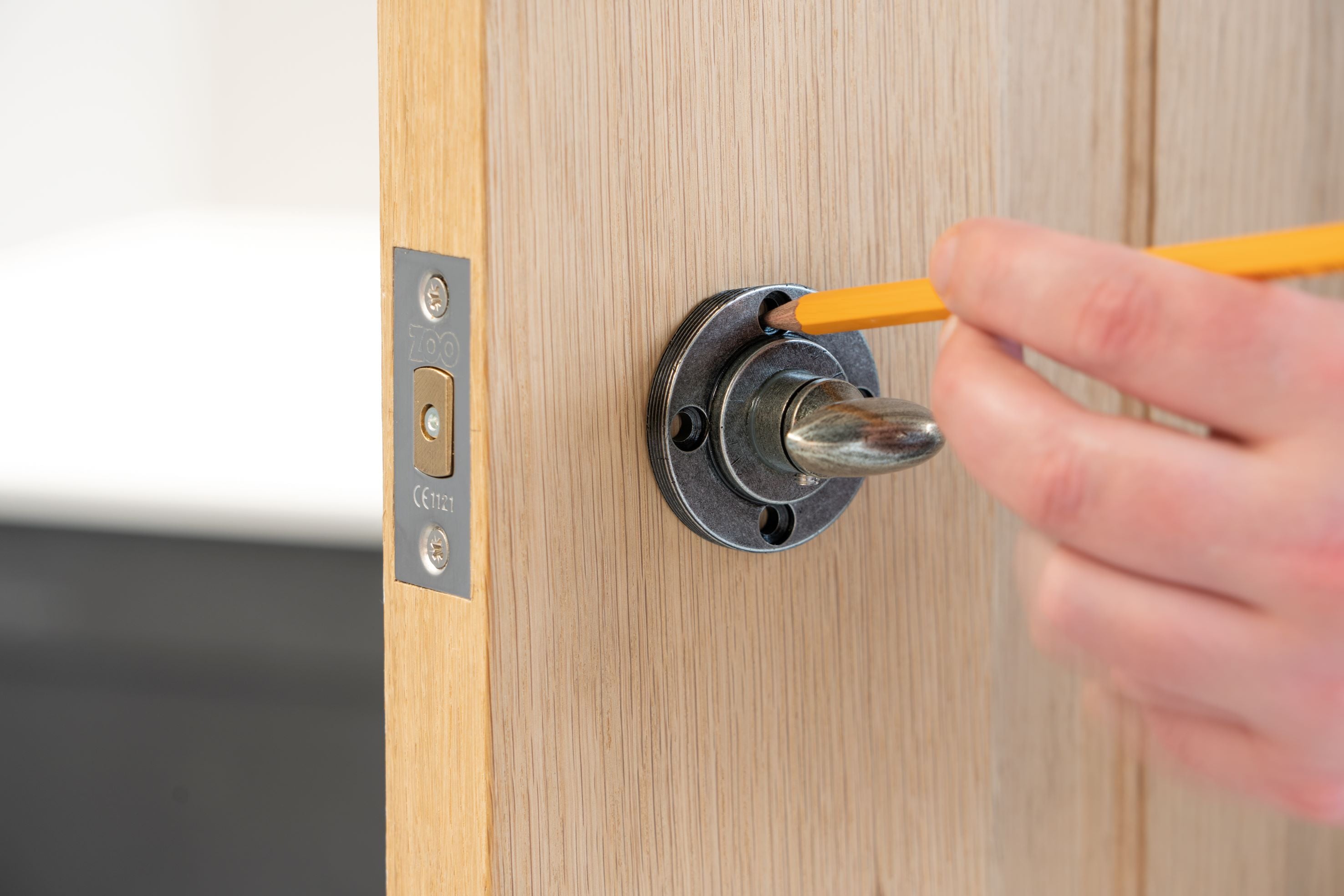 Person using a pencil to mark the position of screwholes on a wooden door for a round, pewter escutcheon