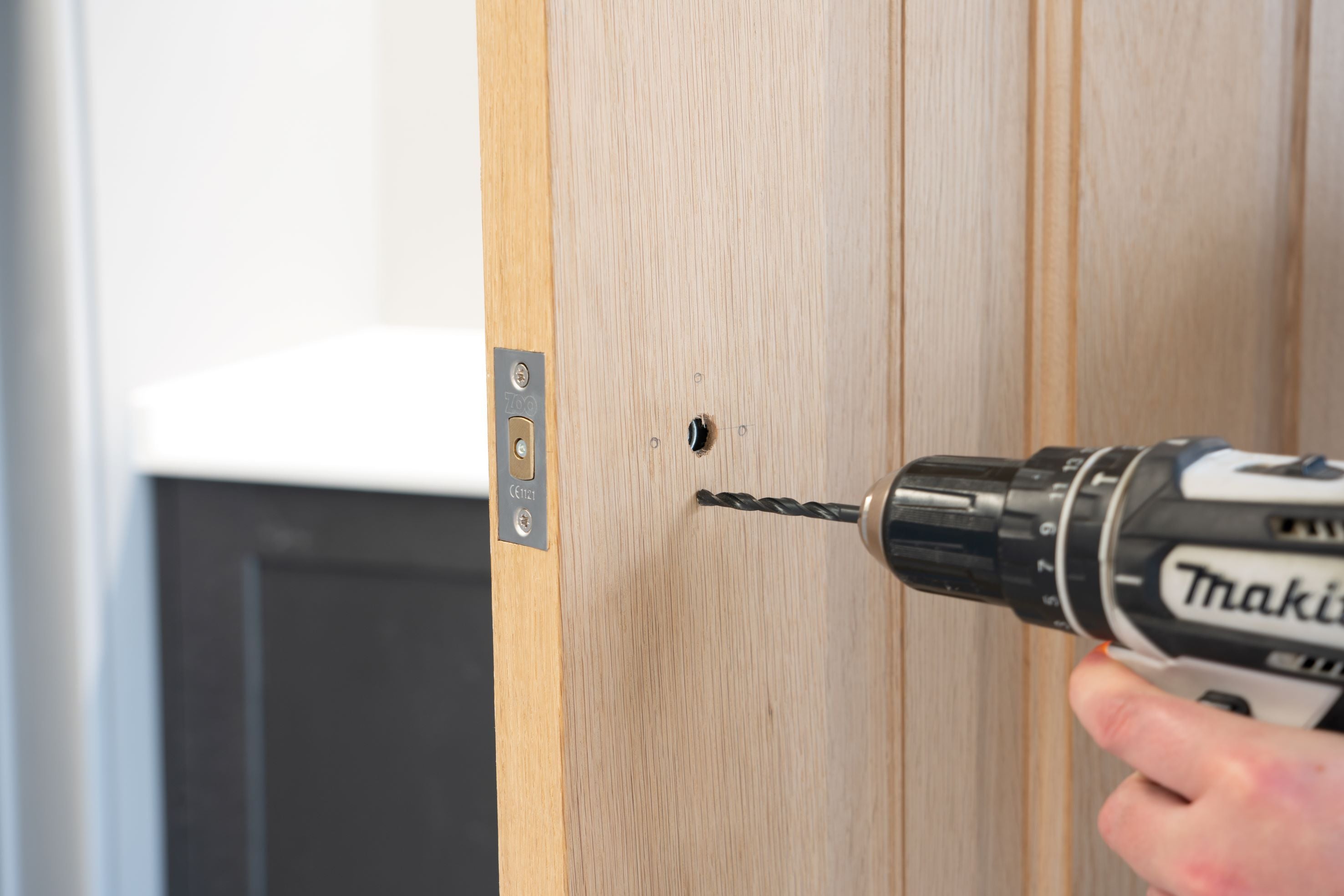 Person using an electric drill to drill a hole into a wooden door for a thumbturn.