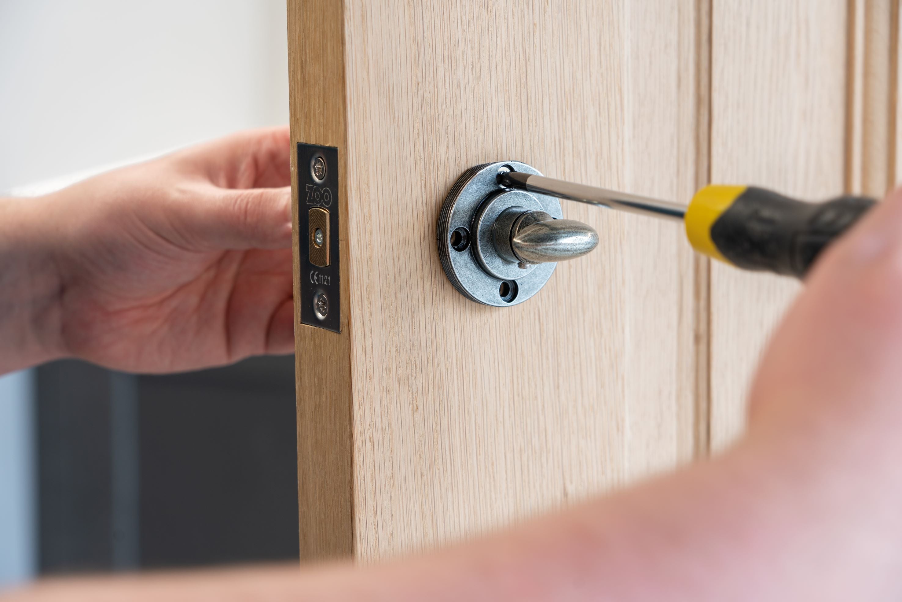Person tightening a screw in the backplate of a Pewter thumbturn on a wooden door.
