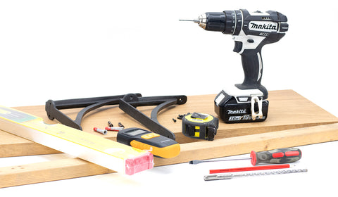 White background image of a Makita drill, From The Anvil shelf brackets, spirit level, screwdriver, planks of wood, metal detector, tape measure, raw plugs, and pencil.