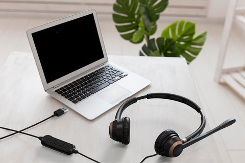 an office desk with a laptop and a double ear wired USB headset on the desk top