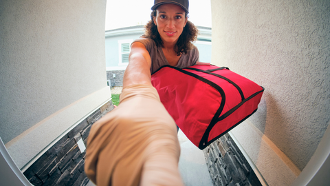 A woman making a food home  delivery pressing a doorbell with food in heat capturing bag