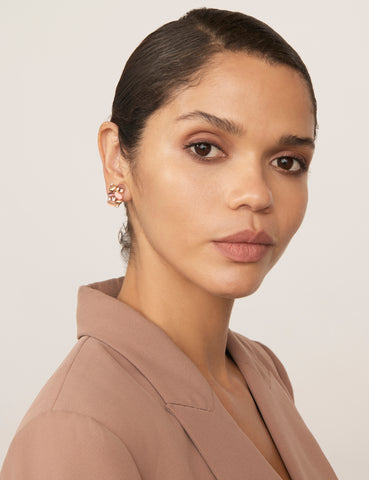 A woman with tan skin and dark hair wears a tan blazer and the Gem Cluster Clip Earrings, featuring mixed pink stones and gold-coloured plating.