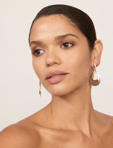 A woman with tan skin and dark hair wears the Layer Drop Window Clip Earrings. Theay feature layered teardrops with cutout accents in gold- and silver-coloured plating.