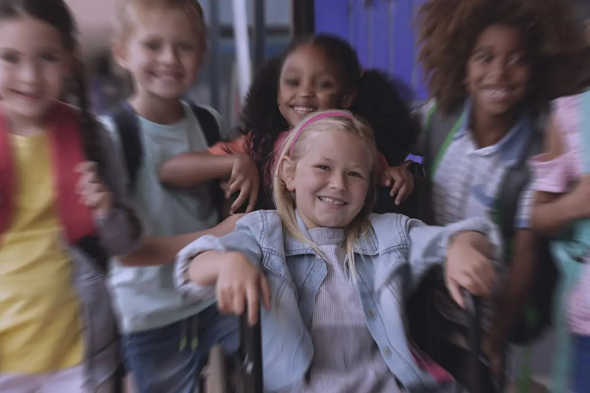 Bambina su sedia a rotelle che sorride circondata dai compagni di classe, in un contesto scolastico inclusivo