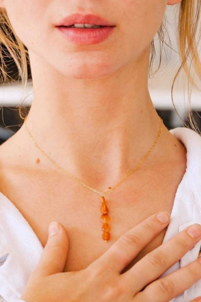 Woman wearing 5 carnelian stones stacked vertically on a delicate gold chain necklace. Each stone measures roughly 3-5mm in diameter.