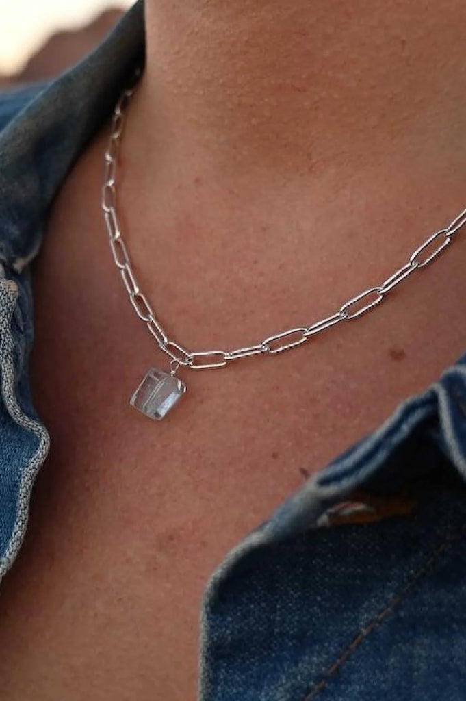 woman wearing a faceted aquamarine crystal on a silver plated link chain necklace.