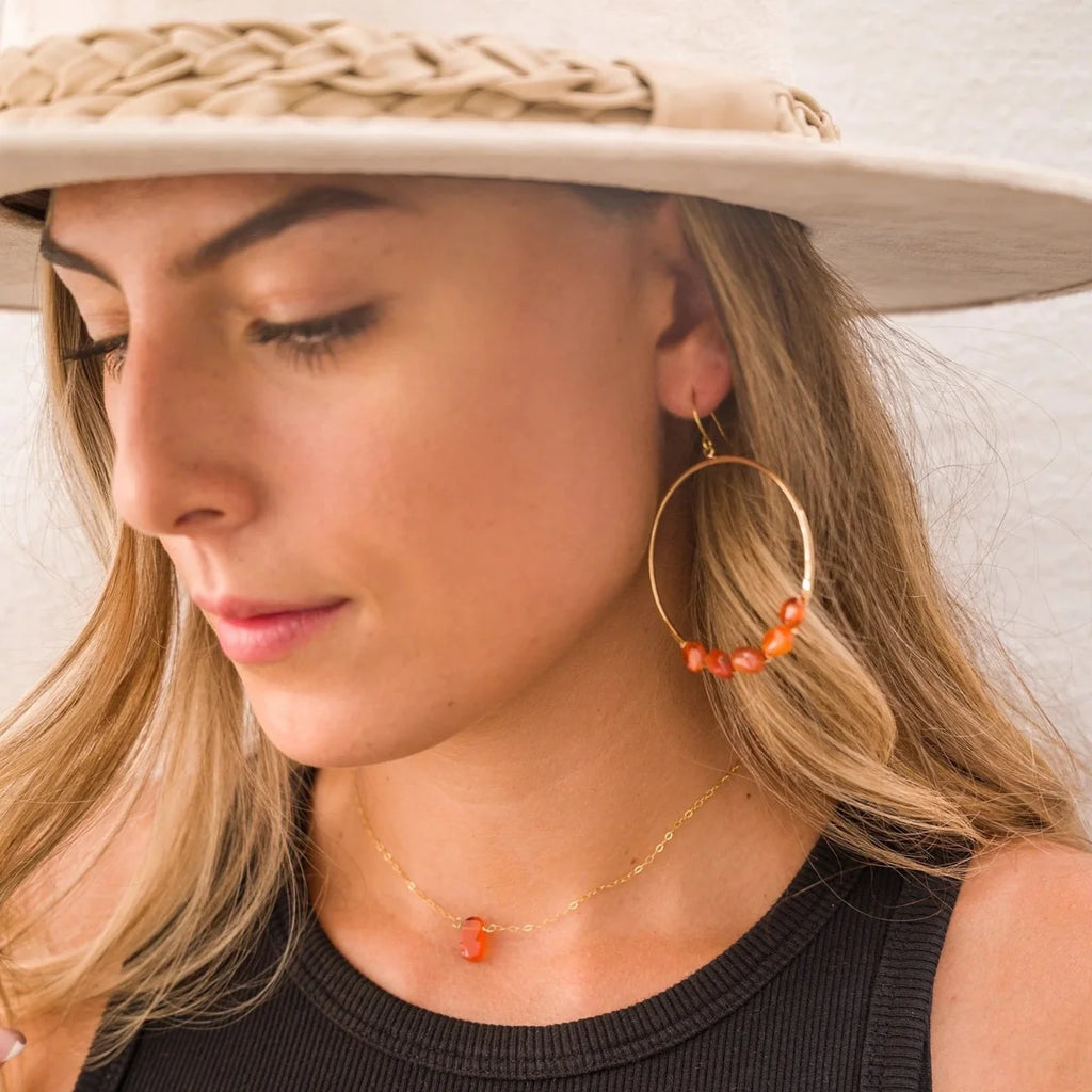 Woman wearing carnelian necklace. The pendant is a polished carnelian stone measuring 1/8" in size on a gold chain.