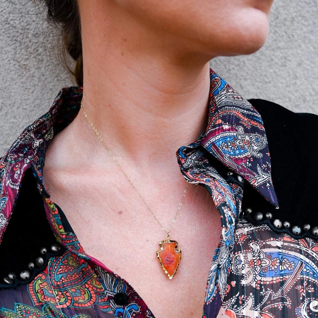 Woman wearing carnelian pendant shaped like an arrowhead with gold electroplating around edges.