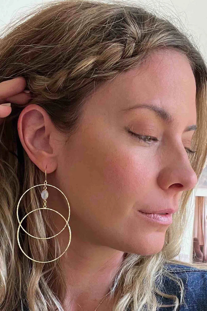 Woman wearing double gold hoop earrings featuring a pink moonstone crystal