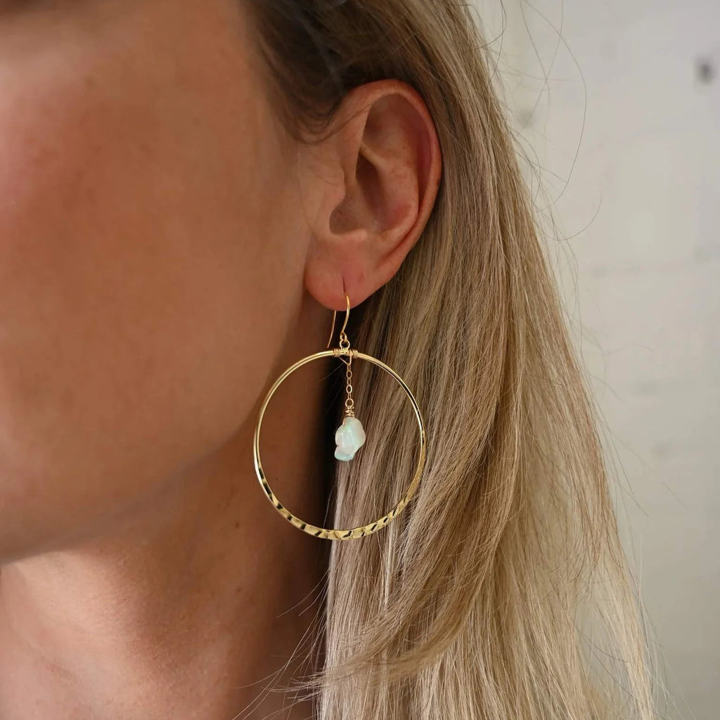 Woman wearing opal gold hoop earrings. Hammered gold hoops with small opal dangling in the middle.