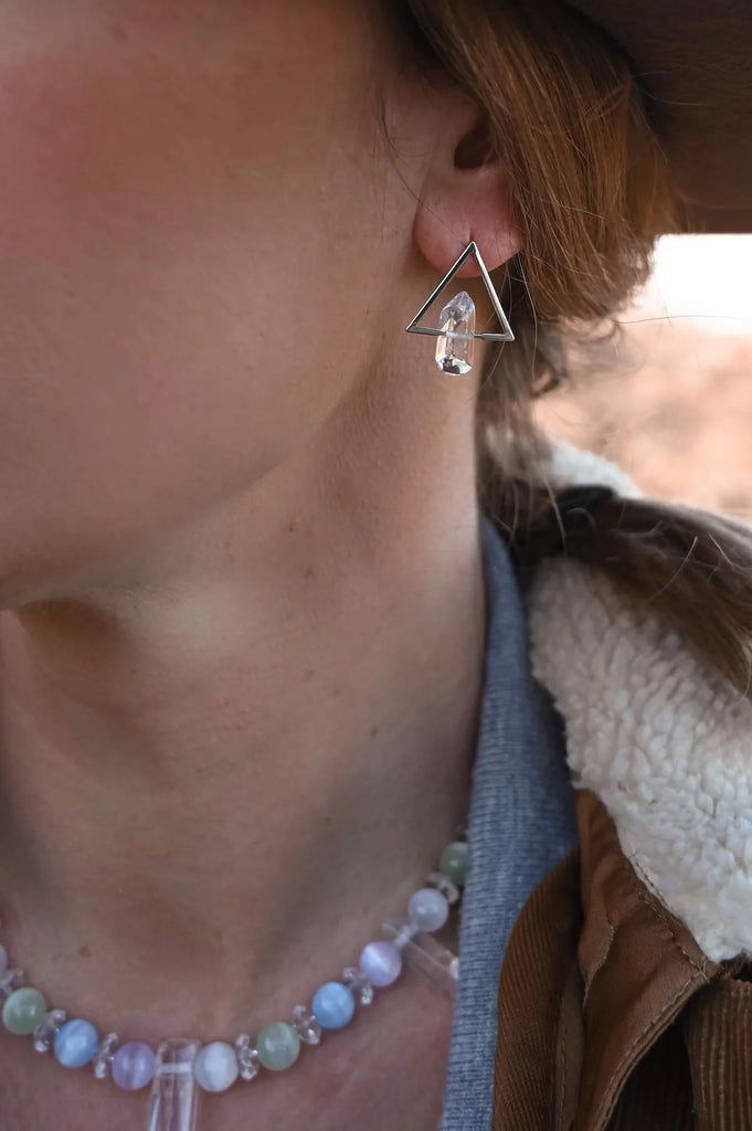 Woman wearing small clear quartz crystal on a triangular silver post-back style earring.