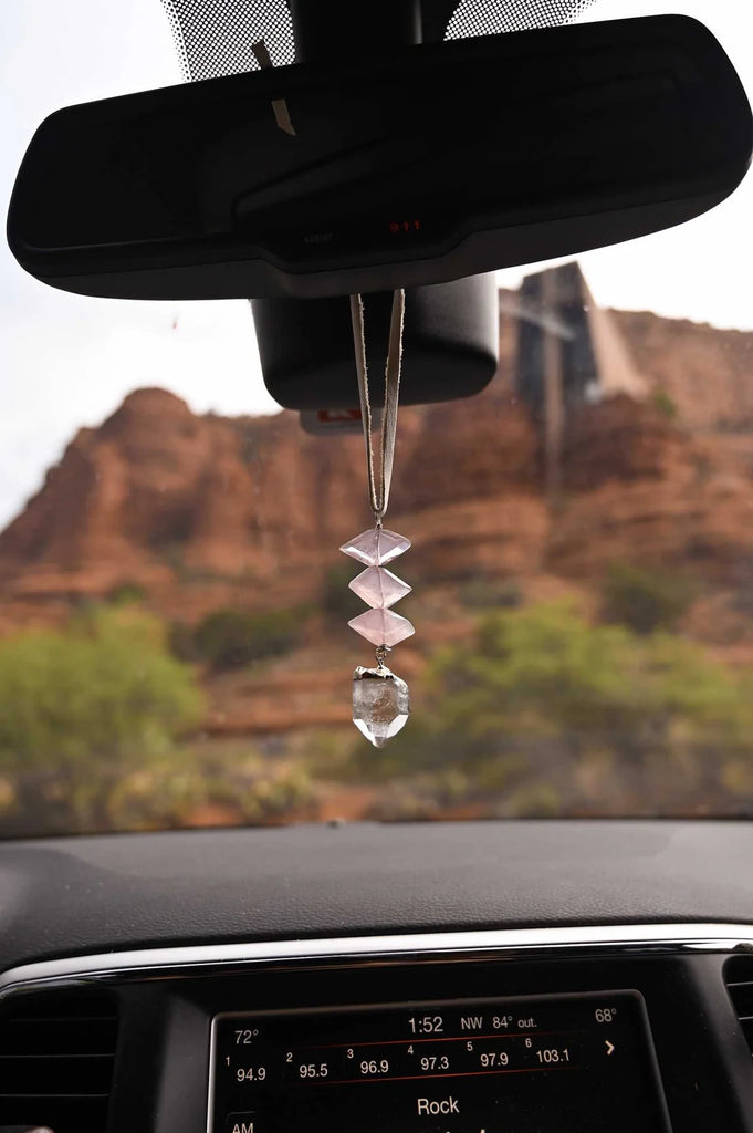 Rose quartz crystal car charm hanging from the rearview mirror on a therapeutic mental health drive in the desert.