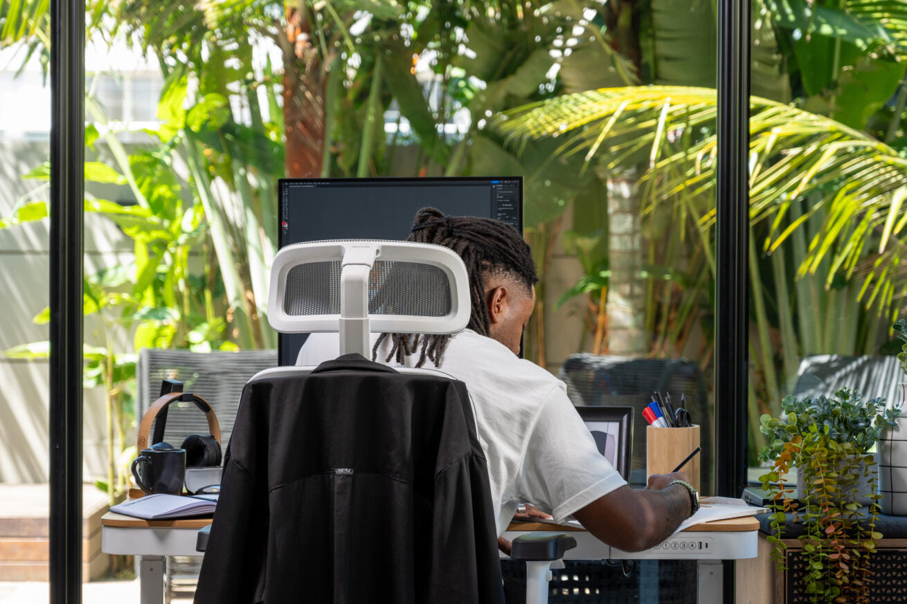 Homem trabalhando em escritório rodeado por plantas e luz natural.