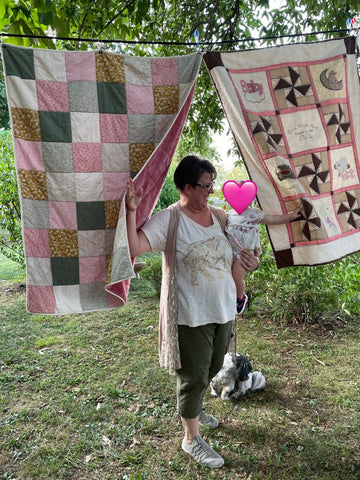 Tondi holding her granddaughter as they walk between two quilts that are hung up outside.