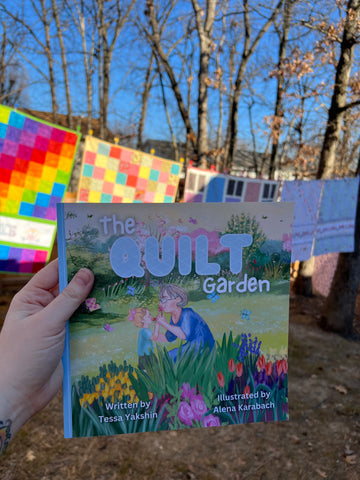 The Quilt Garden children's book being held up in front of some quilts outside