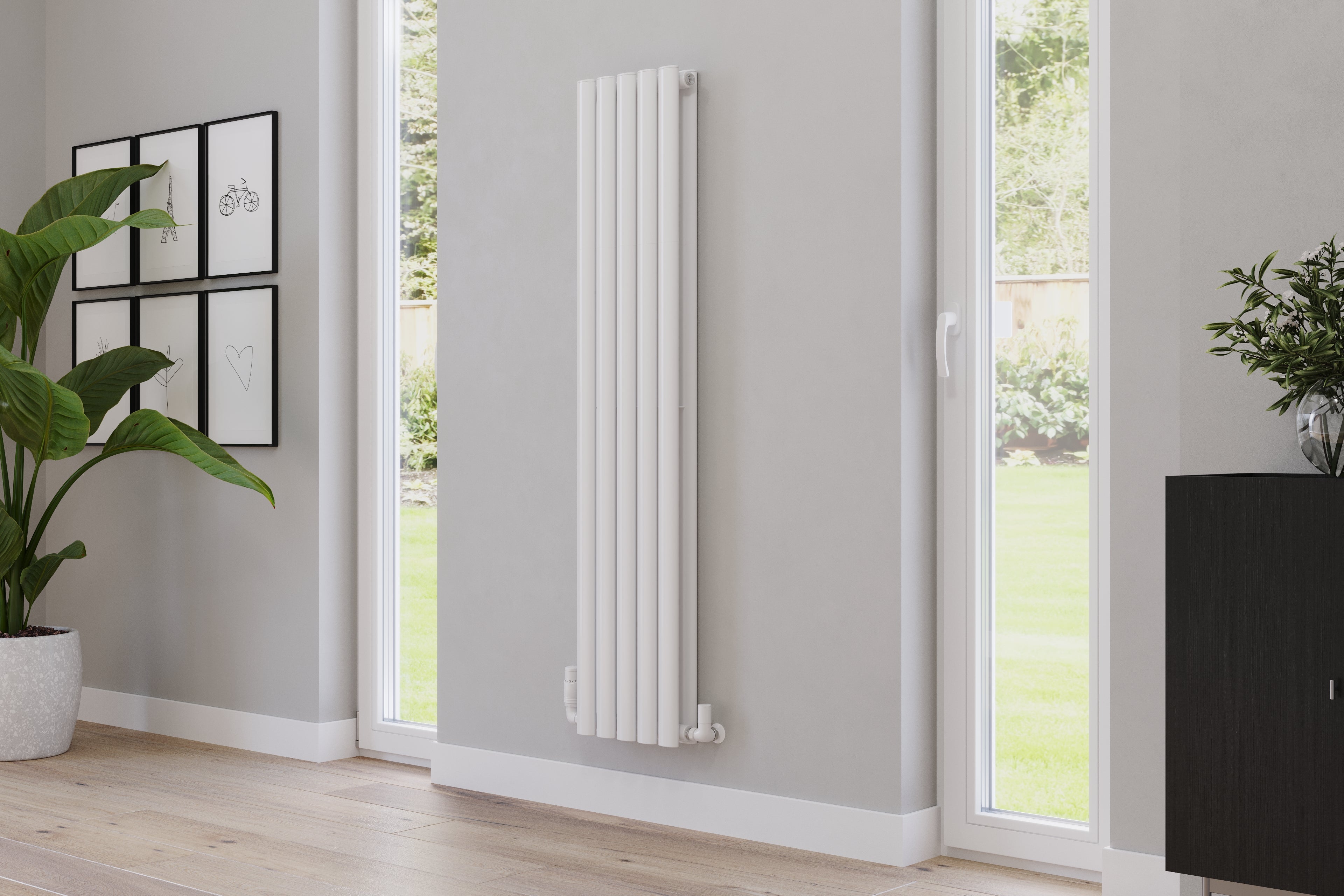 A tall, streamlined, white vertical radiator on a soft grey wall in a Scandi-inspired living room featuring green plants and vertical windows offering plenty of natural light.