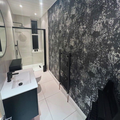 After: A long bathroom featuring stylish white tiles and black and silver vinyl wallpaper, with a black and white sink, toilet, and walk-in shower.