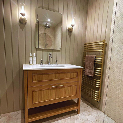 A renovated shower room featuring wood panelling, a wood cabinet, and a gold Crossmoor radiator.