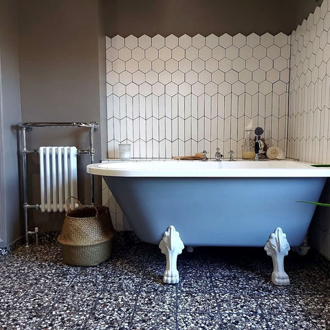 A bathroom with taupe walls and modern floor tiles holds a blue bathtub with white detailing. This matches the traditional white Arundel radiator and the wall tiling.