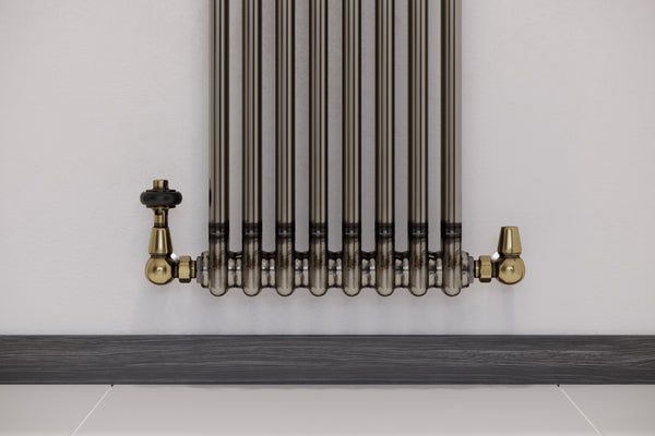 Close-up of a raw metal column radiator with antique brass thermostatic valves.