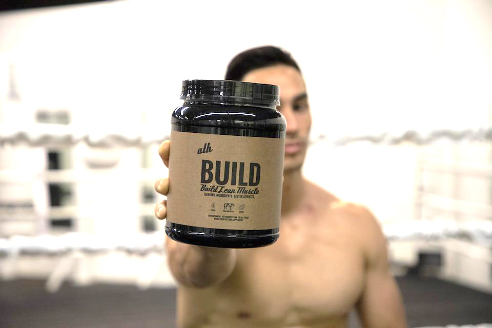 Male athlete holding ATH whey protein in gym. 