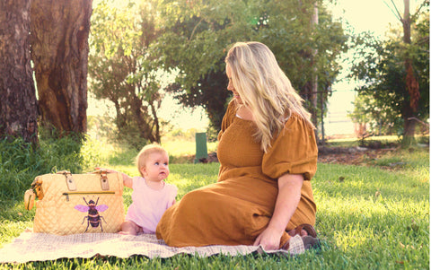 Mother and baby sitting on picnic rug with nappy bag in park