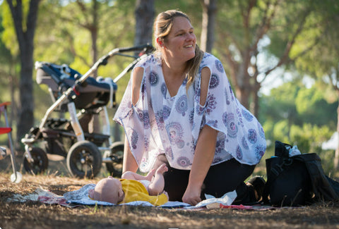 Mother sitting on picnic blanket with baby and pram in park