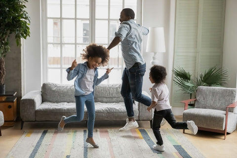 A man and two children joyfully jumping in a living room, strengthening family bonds through musical bonding