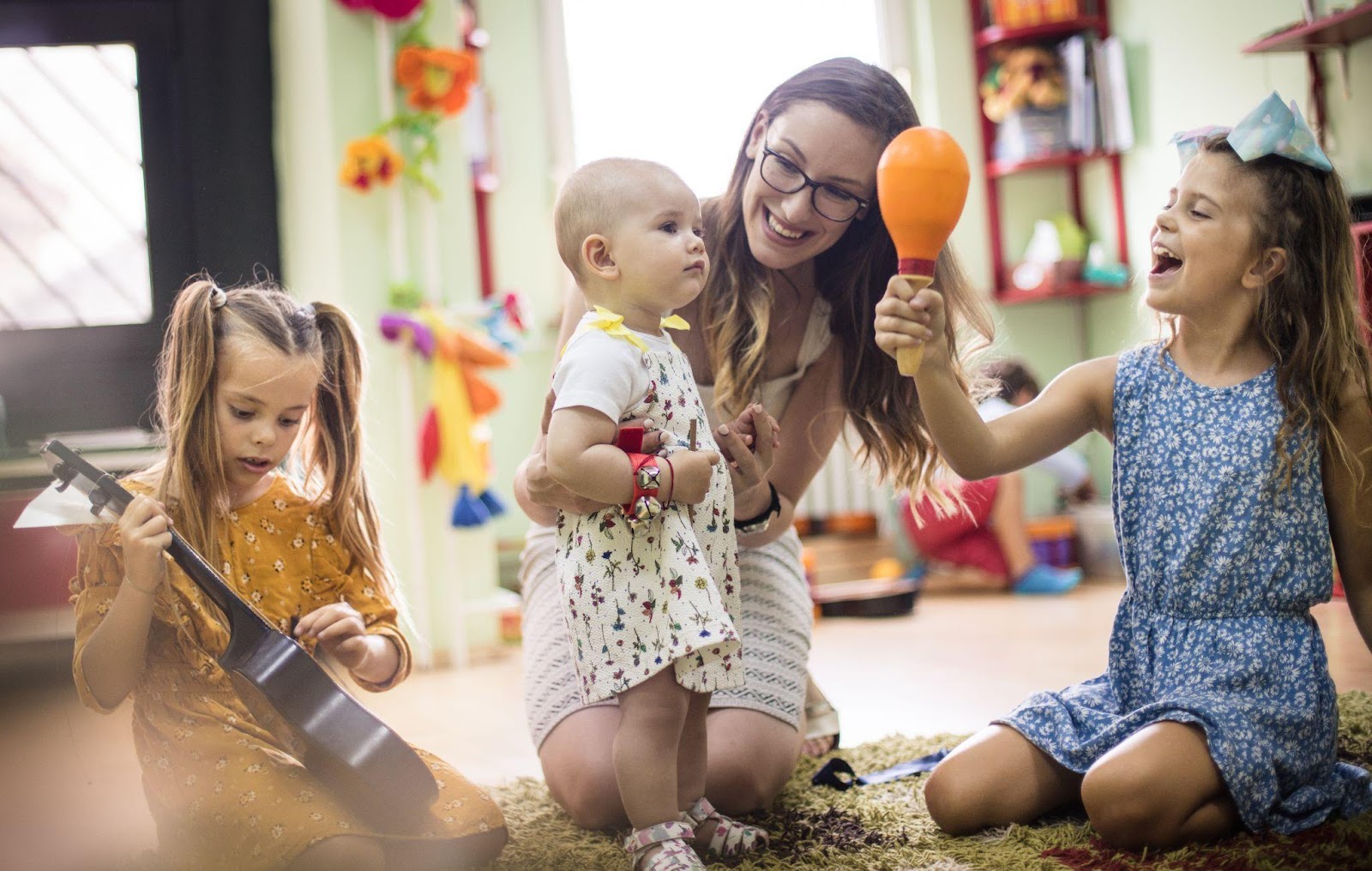 A woman and two children happily playing with toys on the floor.
