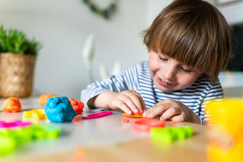 A young boy happily molds play doh with his small hands, letting his creativity flow.