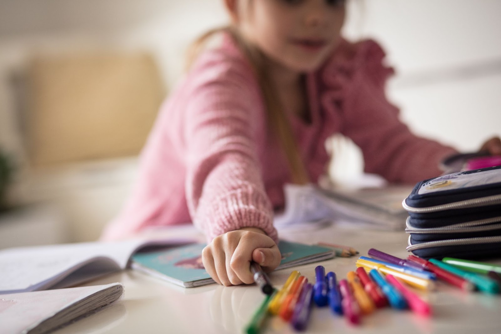 A young girl sits at a table with a notebook and pens