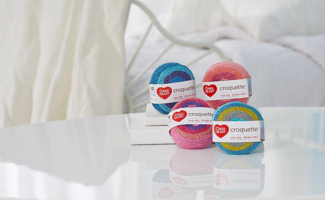 Four Red Heart Croquette yarn is placed on the table top in different colors.