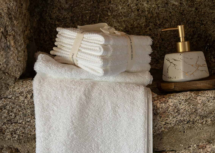 White Egyptian Cotton™ washcloths from THON laid on top of white bath towels from THON on a stone wall ledge next to a marble liquid soap dispenser.