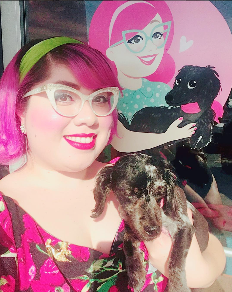 young lady with pink hair and a dog standing in front of a sign that looks like them