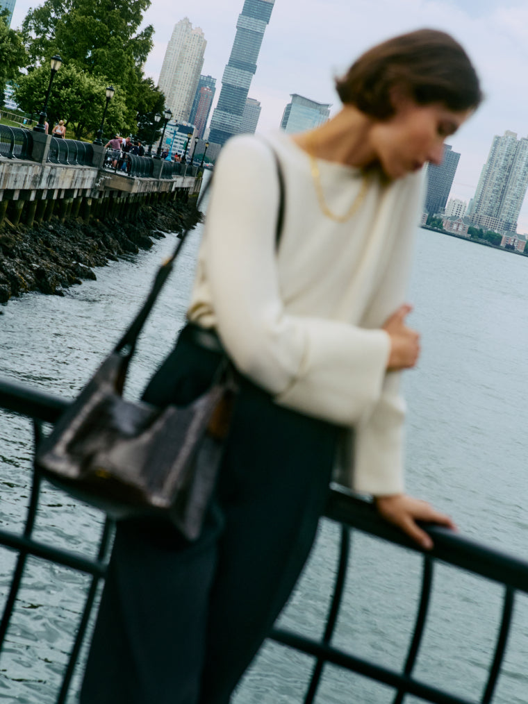 A person leaning on a railing by the waterfront with a cityscape in the background