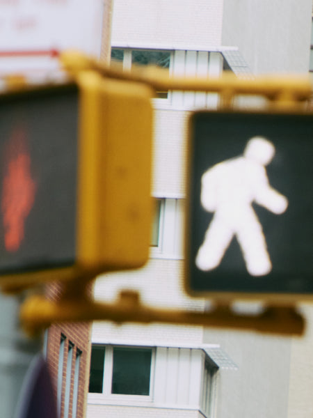 A blurred pedestrian crossing signal with a walking figure, against an urban backdrop