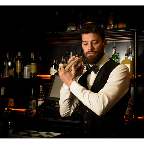 A bartender with a beard and tie is mixing a drink.