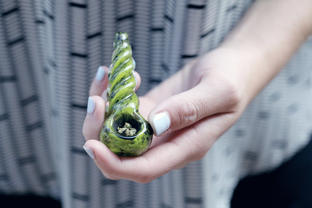 A close up shot of someone holding a green glass bong that's full of cannabis.