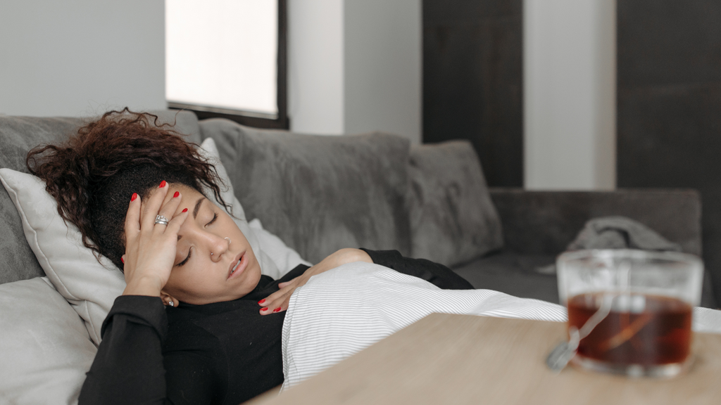 woman laying on couch with a headache and a cup of tea on the table