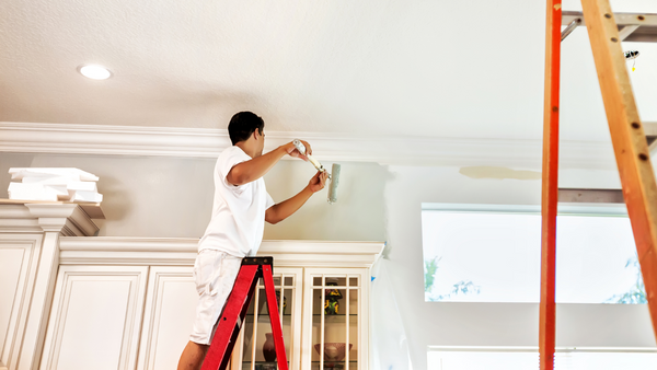 Man standing on ladder painting on top of the kitchen cabinets