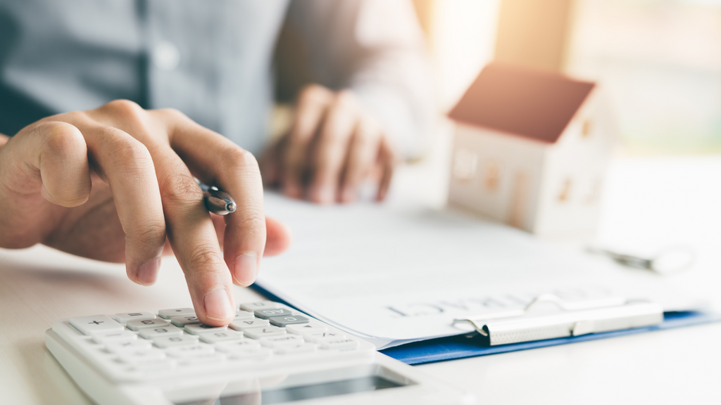 person calculating and budgeting on desk with a mini model of home in the background