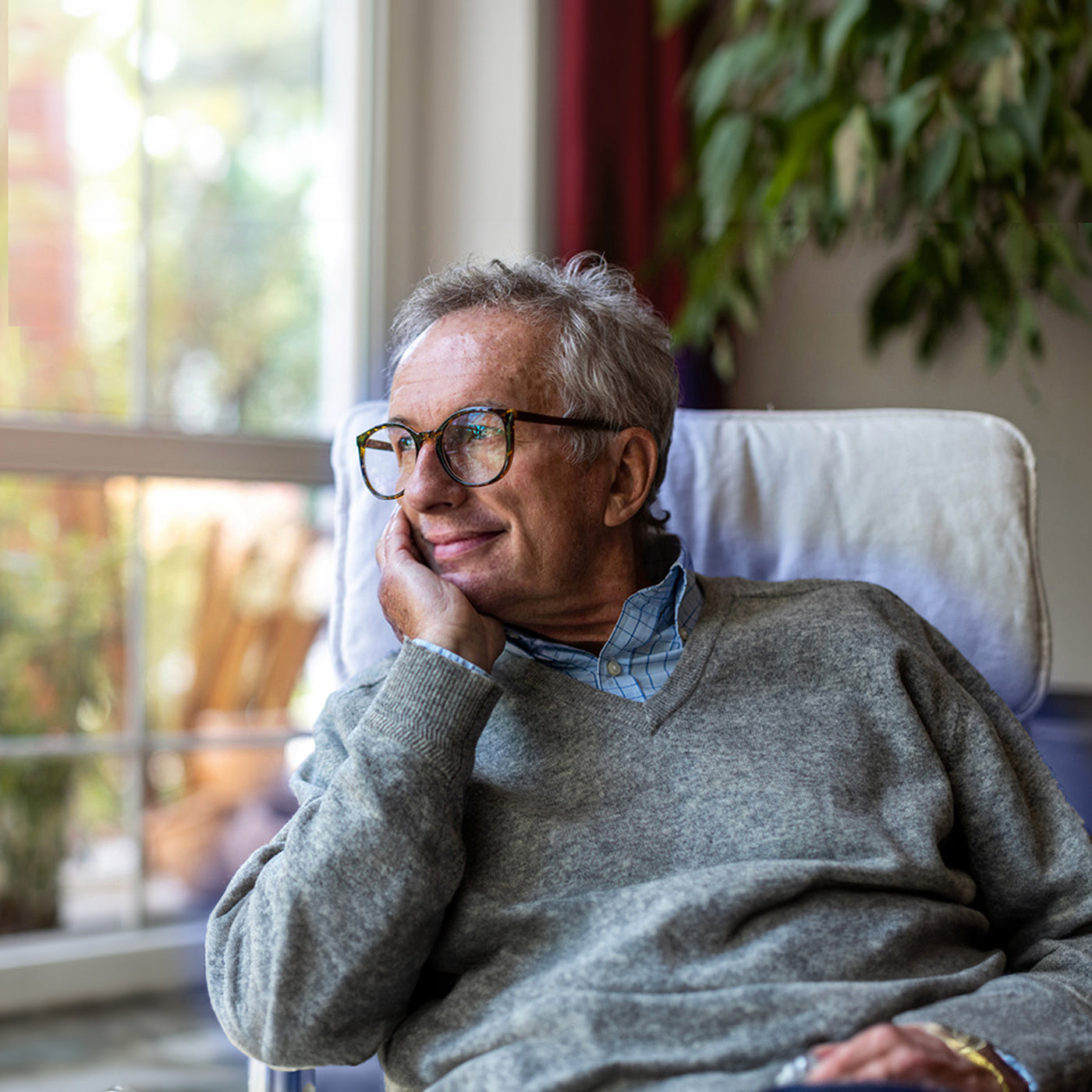 Elderly man. Sat in chair looking out the window with a smile